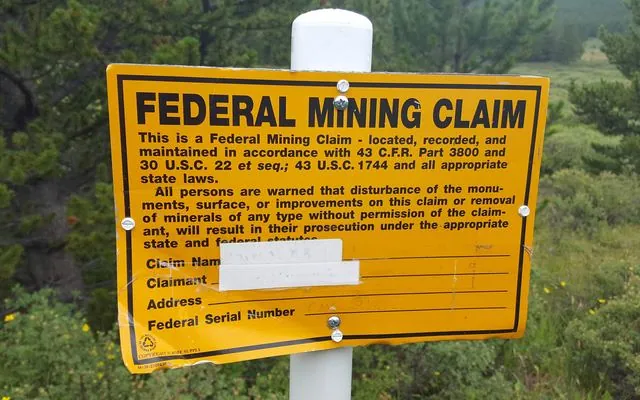 Yellow sign on a post reading FEDERAL MINING CLAIM, with notice text citing federal mining law and blanks for claim name and claimant