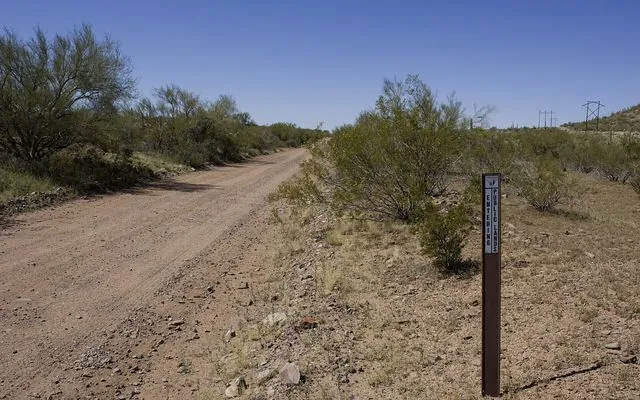 A dirt road through desert scrub with a small brown Entering Public Lands marker post in Ironwood Forest National Monument
