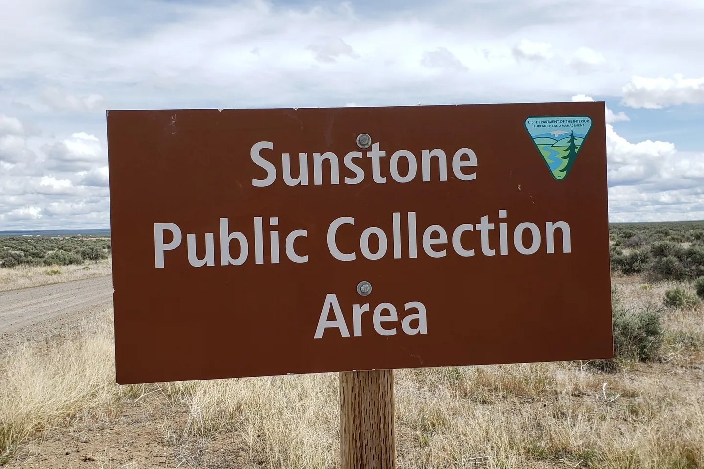 Brown BLM sign reading Sunstone Public Collection Area beside a gravel road in open sagebrush country