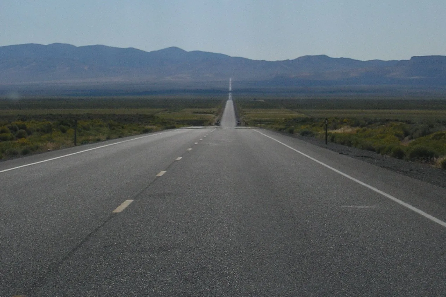Straight highway running across a sagebrush valley toward mountains in central Nevada