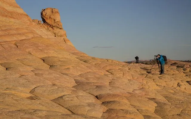 Banded orange sandstone in Vermilion Cliffs National Monument, with a photographer and tripod on the rock